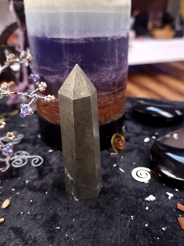 Pyrite Crystal Tower 80mm Short pyrite crystal tower on a black altar cloth before a layered purple candle, with witchy décor and spiral charms around