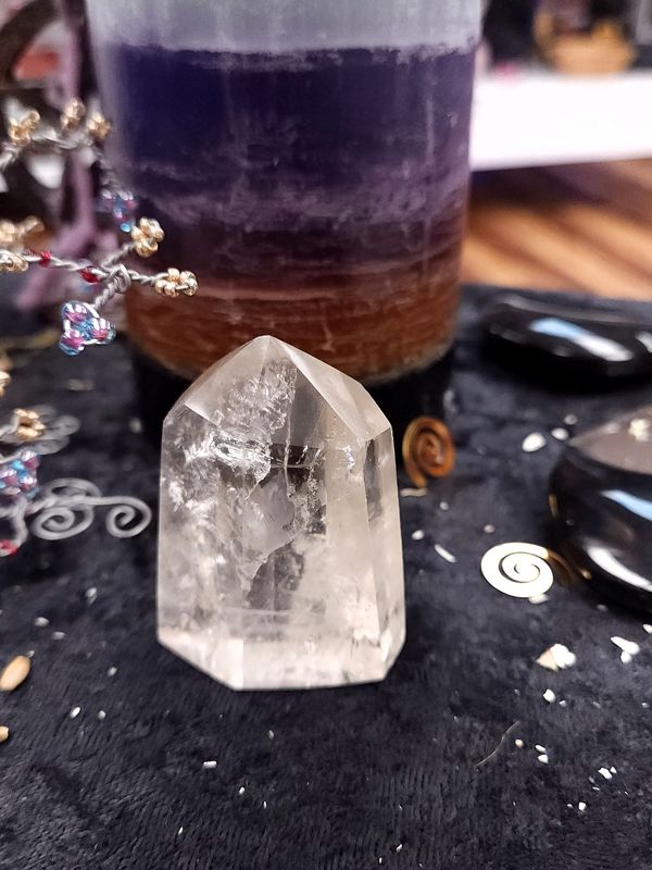 Clear Quartz Crystal Tower 57mm Small clear quartz point on a black altar cloth in front of a purple layered candle with wire gemstone tree and witchy décor