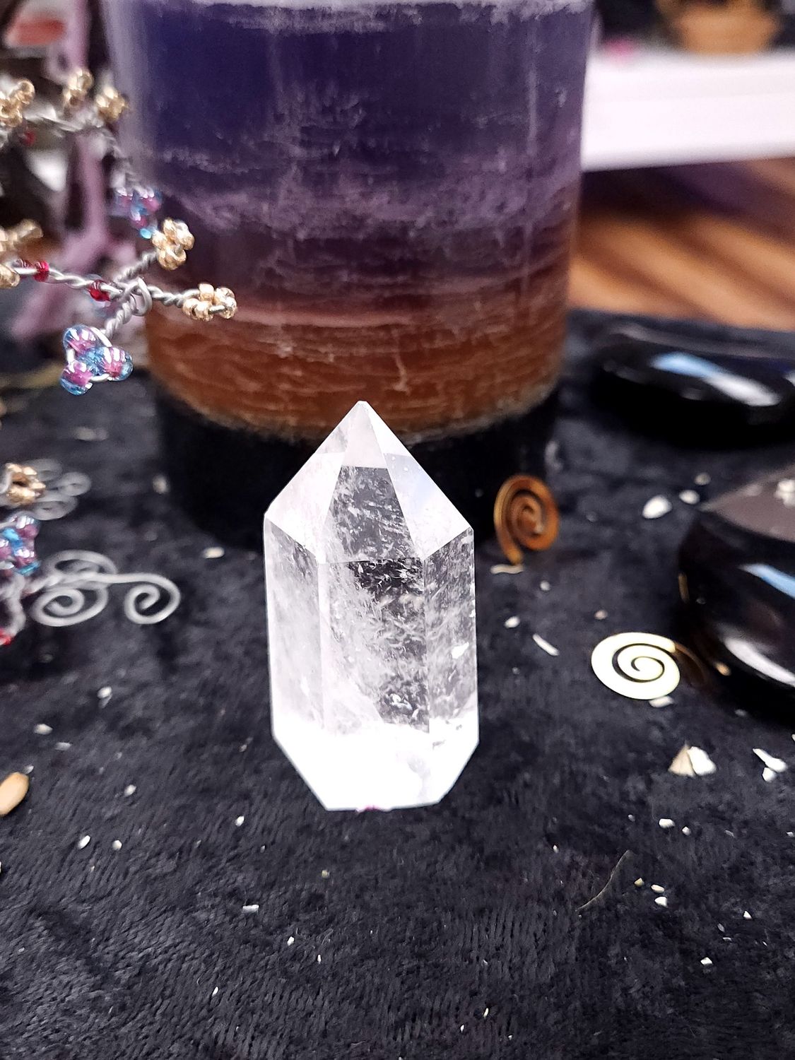 Clear Quartz Crystal Tower 52mm Small clear quartz crystal tower on a black altar cloth in front of a purple layered candle with witchy décor