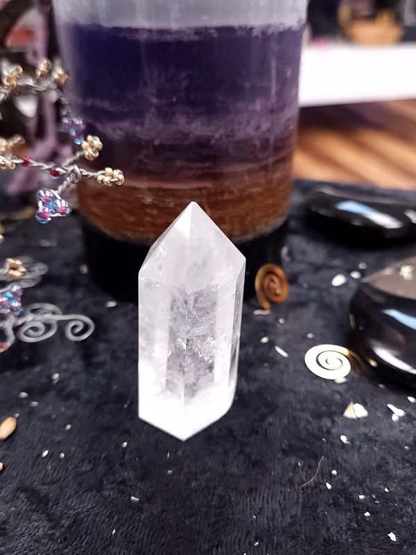 Clear Quartz Crystal Tower 59mm Medium clear quartz crystal tower on a black altar cloth in front of a purple layered candle with wire gemstone tree