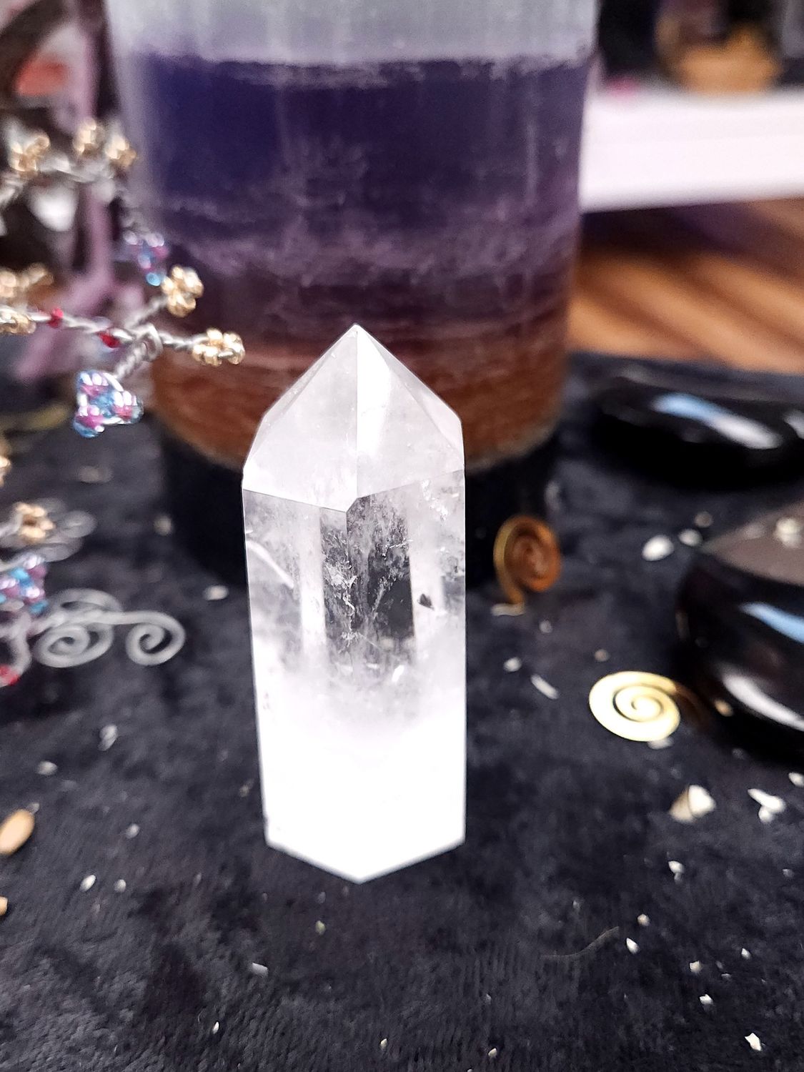 Clear Quartz Generator Tower 58mm Clear quartz generator on a black altar cloth in front of a purple layered candle with wire gemstone tree and spiral charms