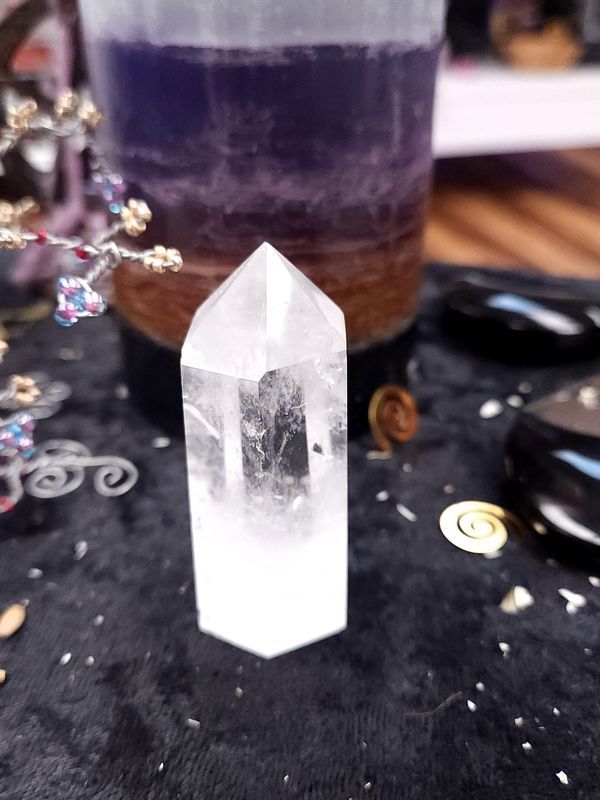 Clear Quartz Generator Tower 58mm Clear quartz generator on a black altar cloth in front of a purple layered candle with wire gemstone tree and spiral charms