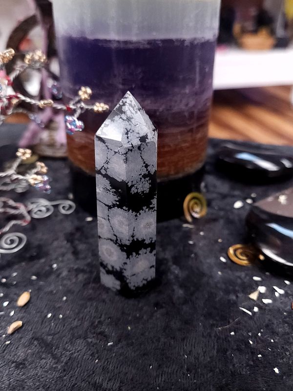 Snowflake Obsidian Crystal Tower 77mm Snowflake obsidian crystal tower with grey “snowflake” patterns on a black altar cloth in front of a purple layered candle