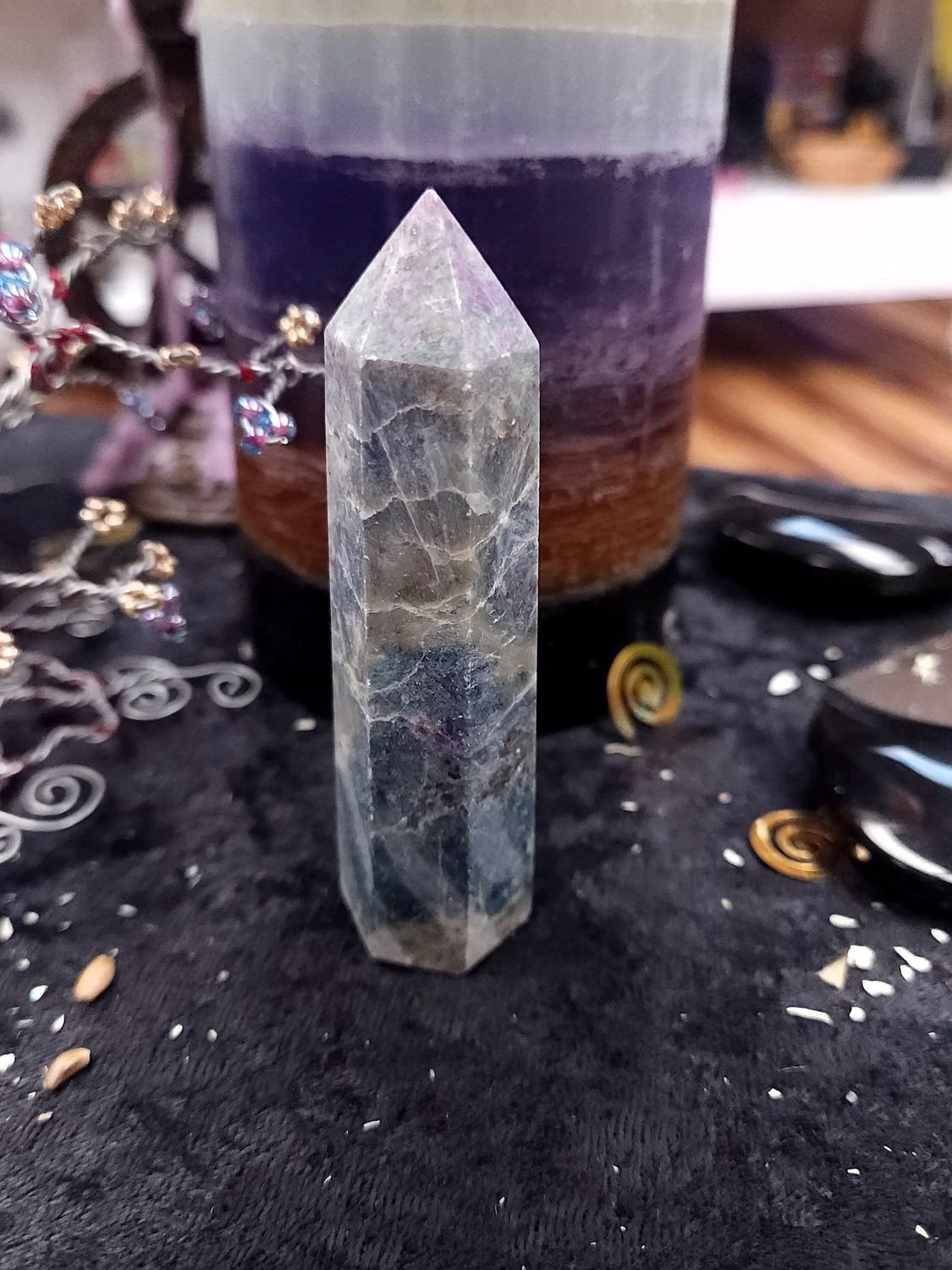 Ruby kyanite crystal tower with blue-grey layers on a black altar cloth in front of a purple layered candle and wire gemstone