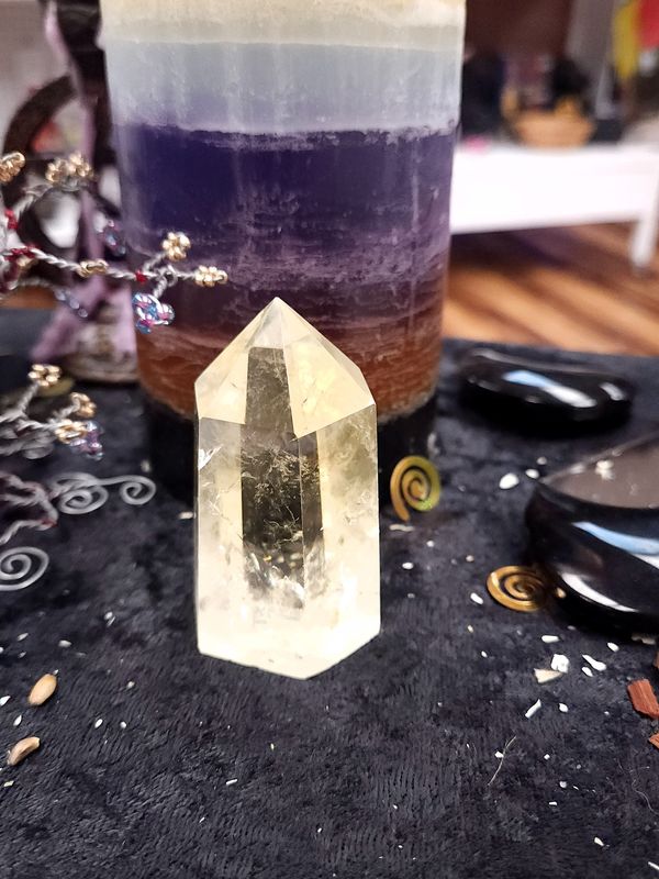 Natural Citrine Crystal Tower 66mm Medium natural citrine crystal tower on a black altar cloth in front of a purple layered candle with spiral charms