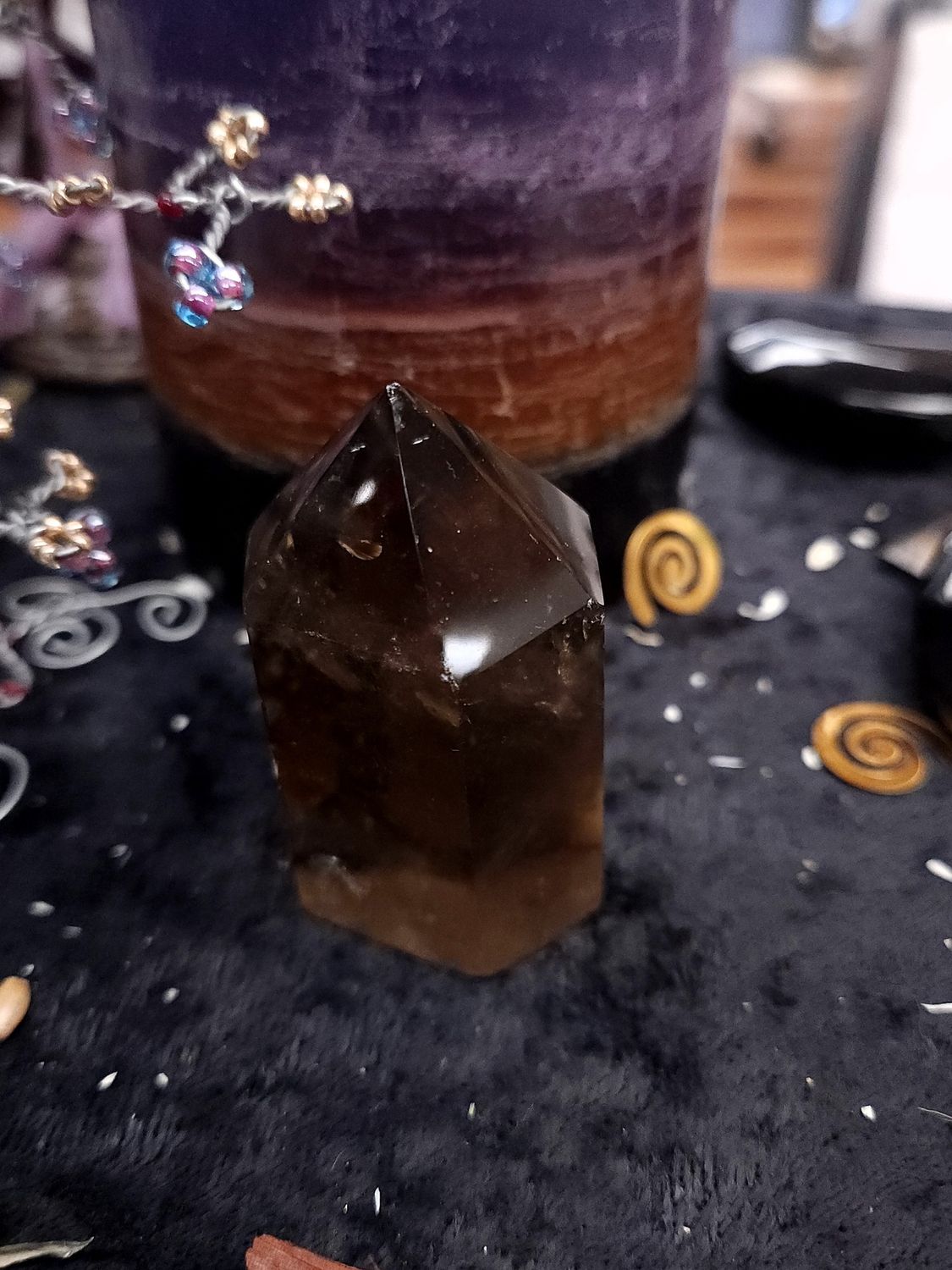 Smoky Quartz Crystal Tower 57mm Smoky quartz crystal tower on a black altar cloth in front of a purple layered candle with wire gemstone tree and spirals