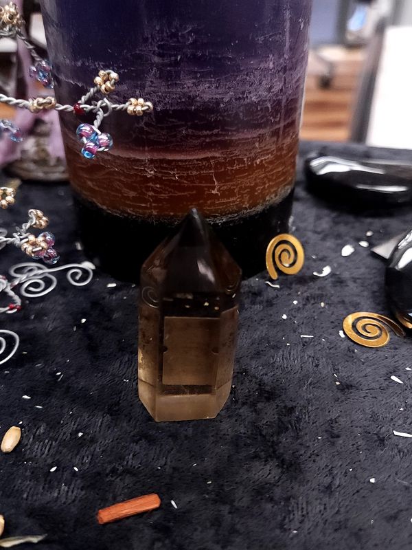 Smoky Quartz Crystal Tower 52mm Small smoky quartz crystal tower on a black altar cloth in front of a purple layered candle with wire gemstone tree nearby.