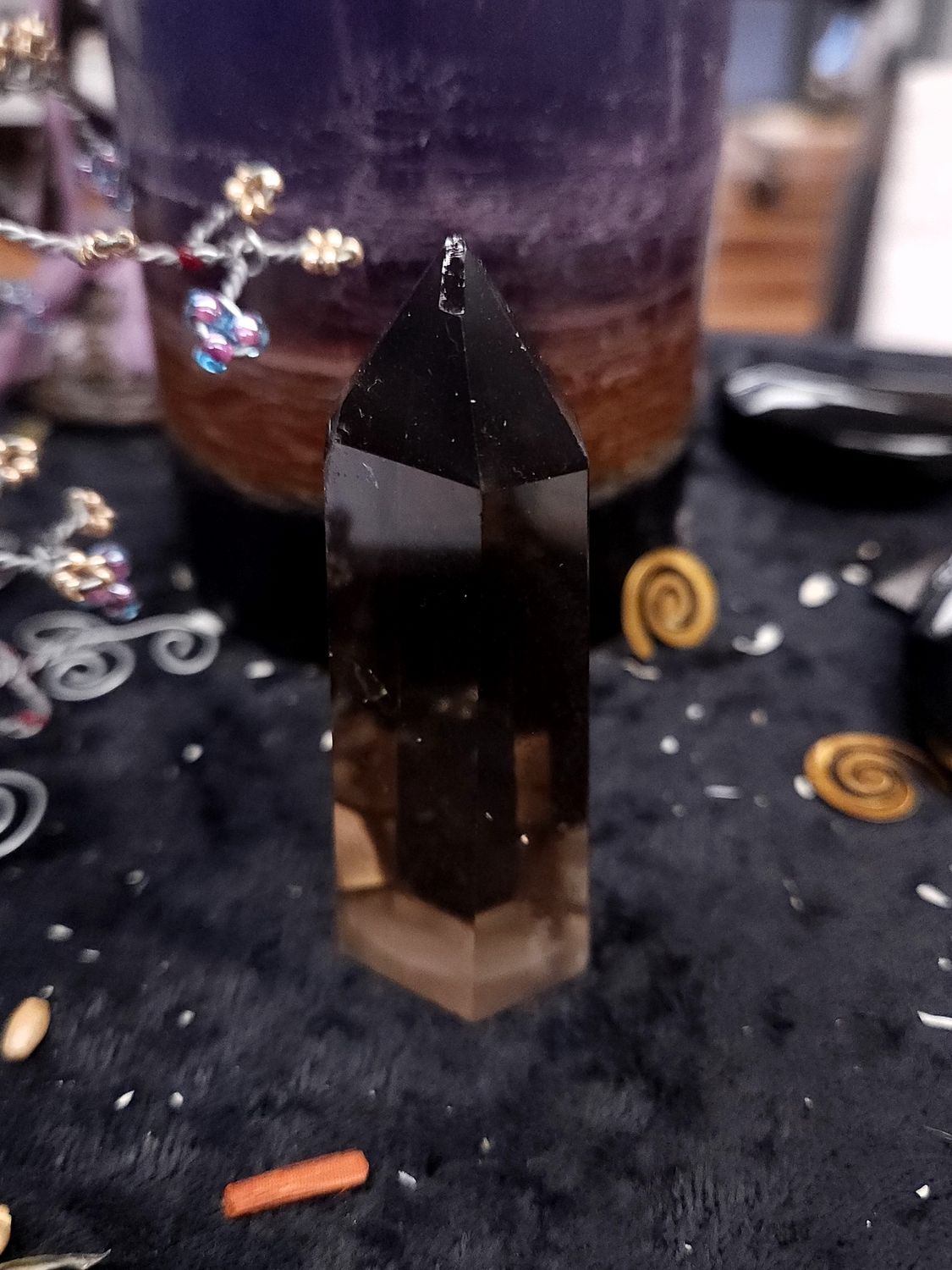 Smoky Quartz Crystal Tower 71mm Tall smoky quartz crystal tower, dark at the tip and lighter at the base, on a black altar cloth in front of a striped candle