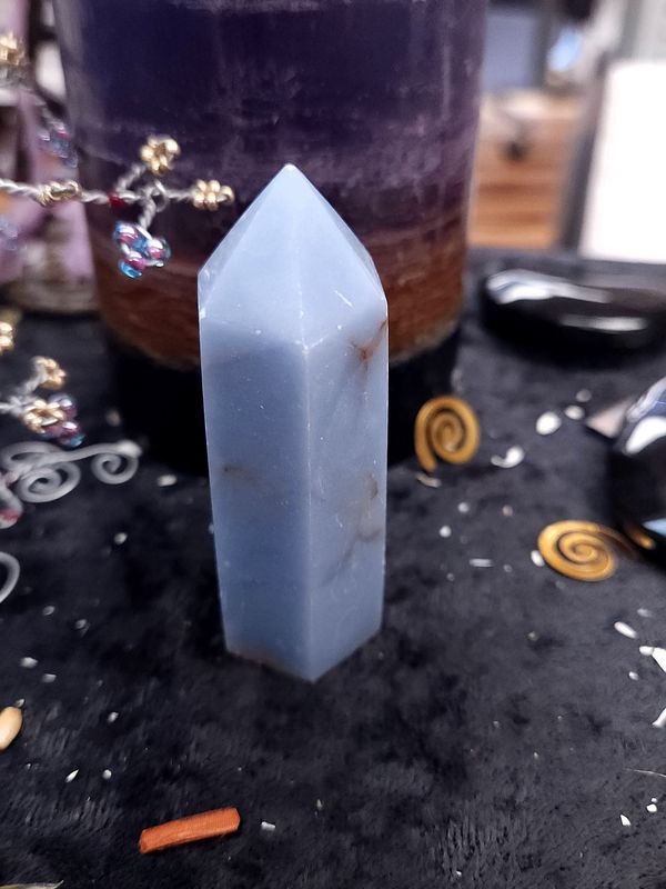 Angelite Crystal Tower 73mm Tall blue angelite crystal tower with small brown inclusions on a black altar cloth in front of a purple layered candle