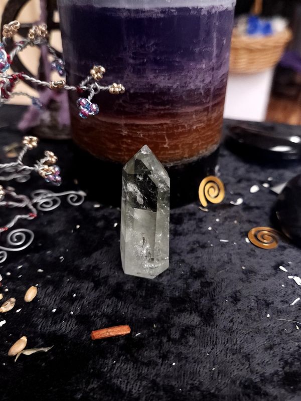 Green Quartz Crystal Tower 51mm Small green quartz crystal tower on a black altar cloth in front of a purple layered candle with wire gemstone tree