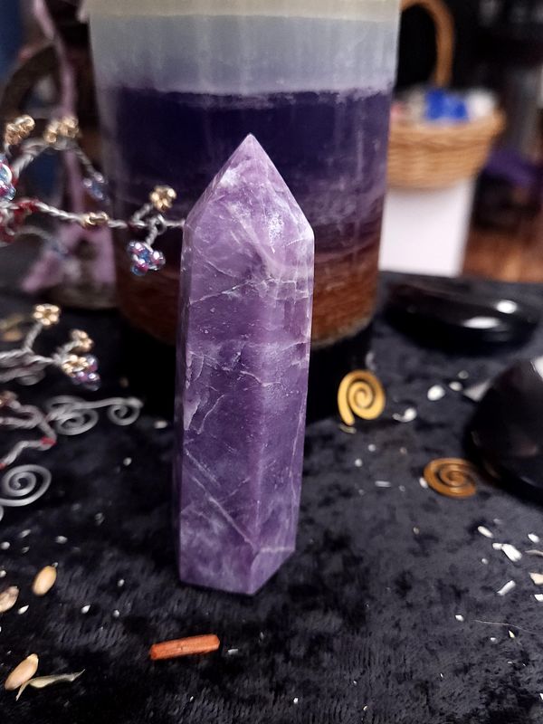 Lepidolite Crystal Tower 86mm Purple lepidolite crystal tower on a black altar cloth in front of a purple layered candle with wire gemstone tree