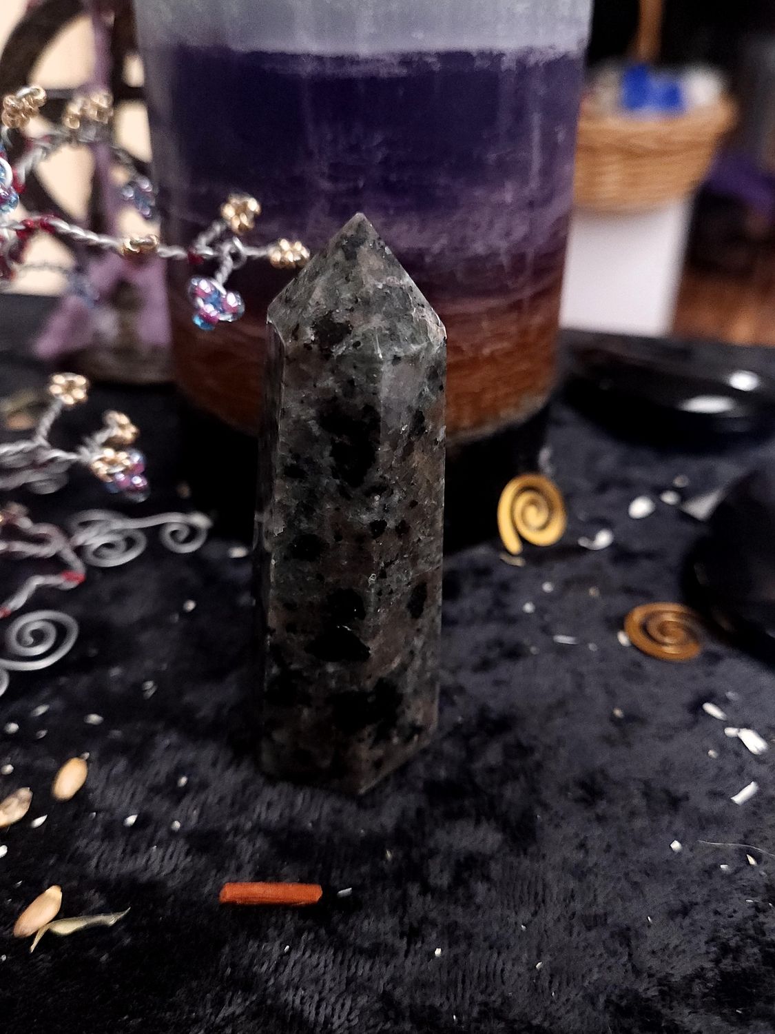 Grey and black yooperlite crystal tower on a black altar cloth in front of a purple layered candle with wire gemstone tree