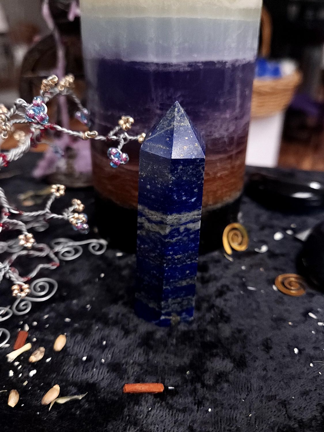 Lapis Lazuli Tower 81mm Royal blue lapis lazuli crystal tower with gold flecks and light bands on a black altar cloth in front of a purple candle
