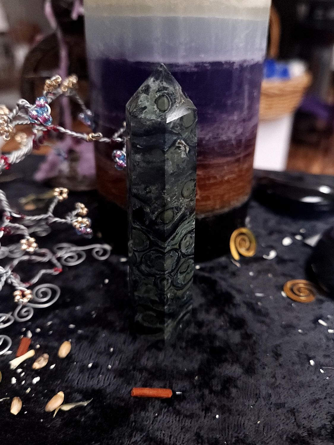 Tall kambaba jasper crystal tower with dark green circular patterns on a black altar cloth in front of a purple candle