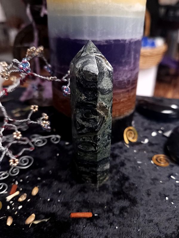 Kambaba Jasper Crystal Tower 92mm Tall kambaba jasper crystal tower with dark green and black circular patterns on a black altar cloth in front of a candle