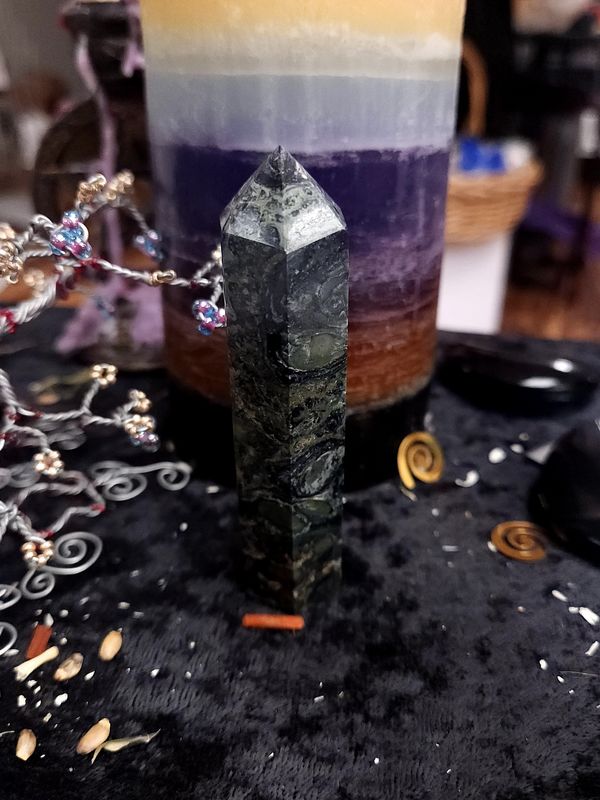 Kambaba Jasper Crystal Tower 94mm Tall kambaba jasper tower with green fingerprint-like swirls on a black altar cloth in front of a purple layered candle
