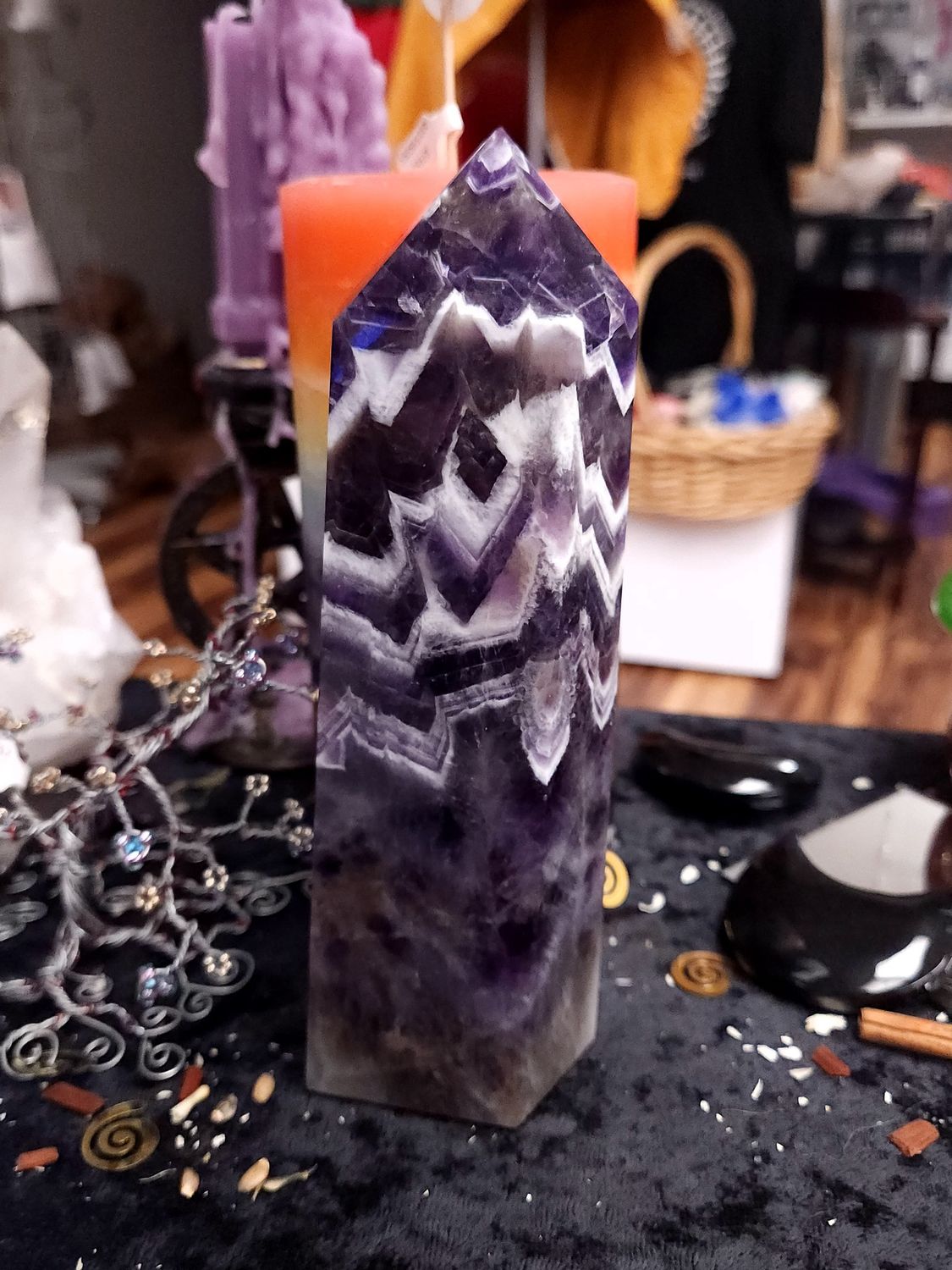 Tall chevron amethyst crystal tower with bold white and purple V-shaped bands on a black altar cloth in front of a candle