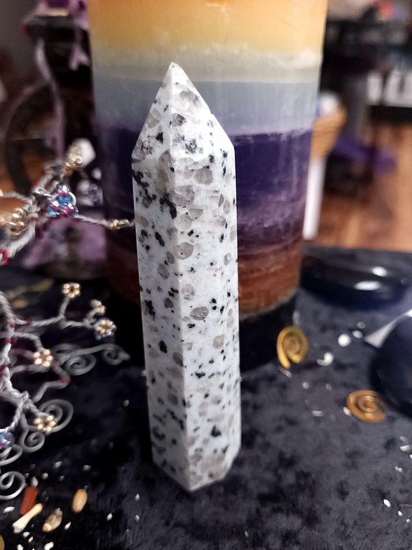 Kiwi Jasper Crystal Tower 109mm Tall pale kiwi jasper crystal tower with grey and black speckles on a black altar cloth in front of a rainbow-purple candle