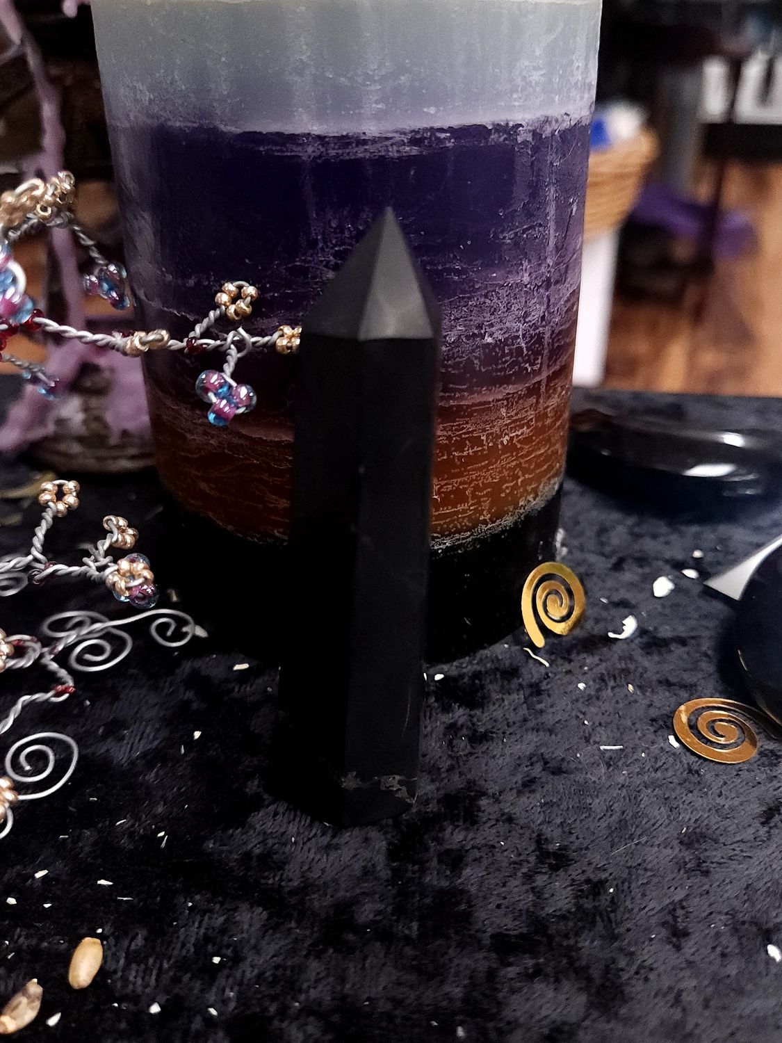Small black shungite crystal tower on a black altar cloth in front of a purple layered candle with wire gemstone tree
