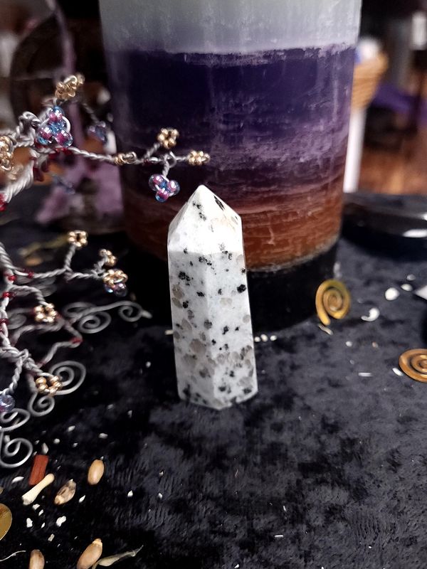 Kiwi Jasper Crystal Tower 61mm Small kiwi jasper crystal tower with grey and black speckles on a black altar cloth in front of a purple layered candle