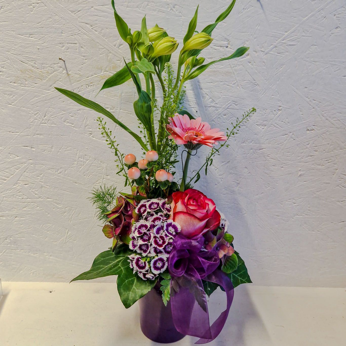 Kräftige Farben: gestuftes Gesteck purpur/rosa/grün mit Schleife