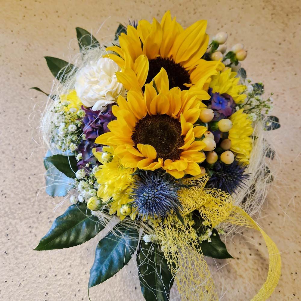 Gesteck mit Sonnenblumen und Disteln, in Korb