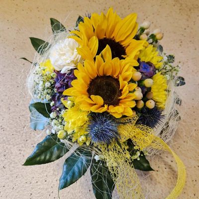 Gesteck mit Sonnenblumen und Disteln, in Korb