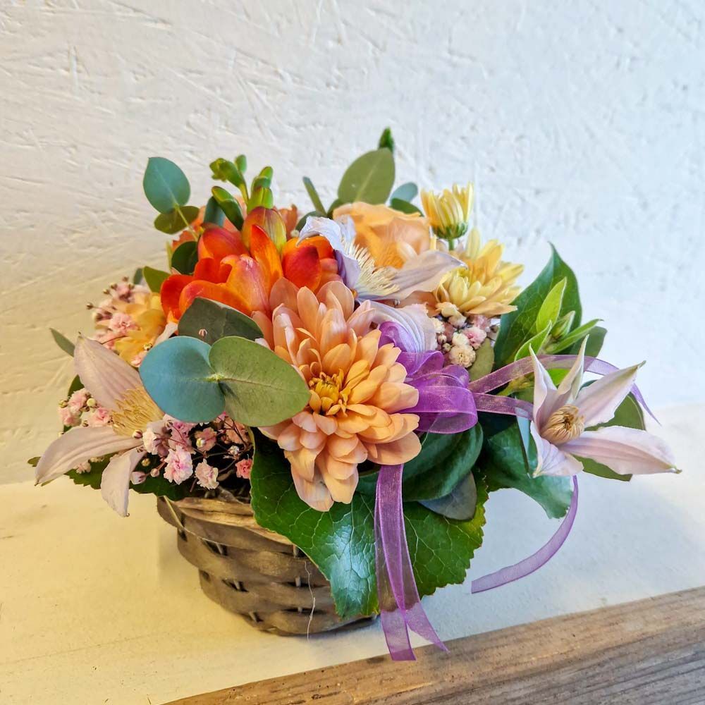 Fröhliches Gesteck mit kleiner Schleife in Korb, gemischte Farben und verschiedene Blätter Fröhliches Gesteck mit kleiner Schleife in Korb, gemischte Farben und verschiedene Blätter