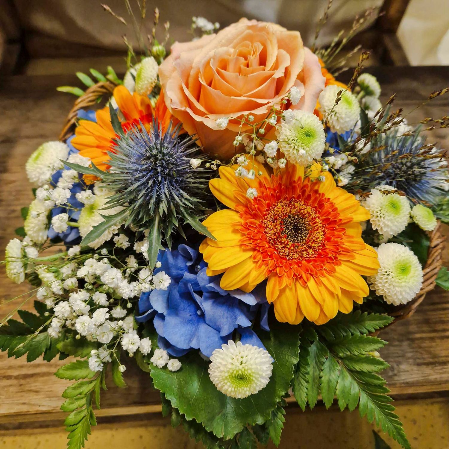 Gesteck mit Rose, Gerbera und Disteln, in Korb