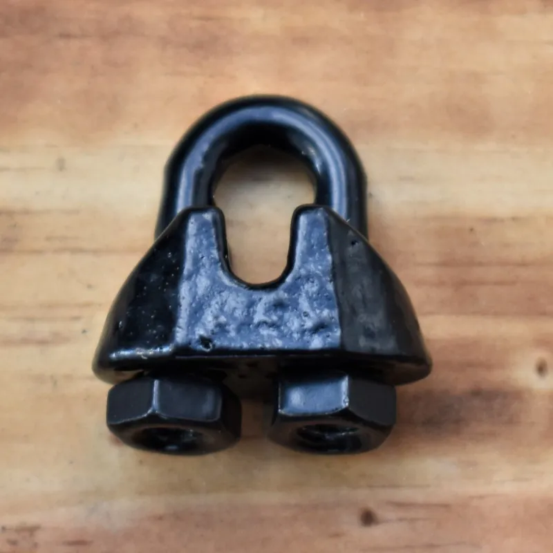 Close-up of a 1/16 inch wire rope clip with black powder-coated finish, resting on a wooden surface.