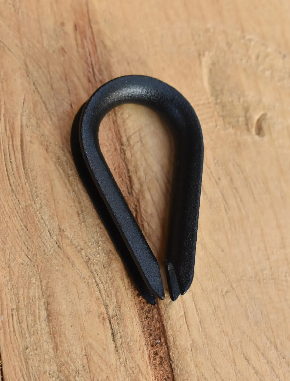 Close-up of 1/8 inch wire rope thimble with custom powder coated finish, placed on natural wood surface.