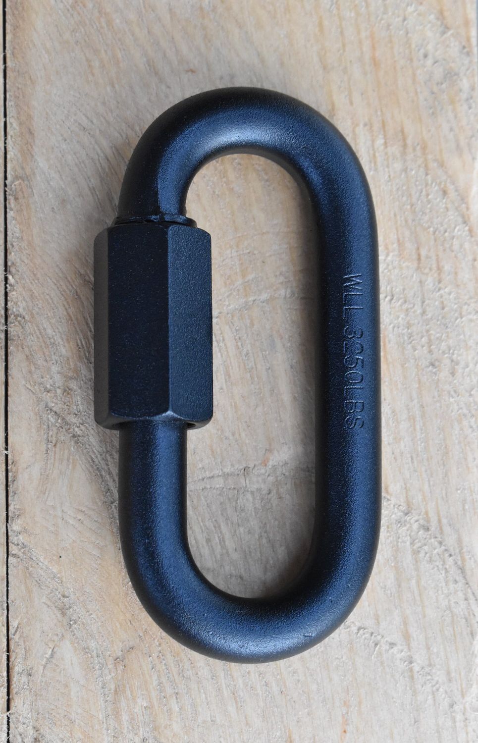 Close-up of a 1/2 inch quick link metal connector with threaded screw lock, resting on a wood background.