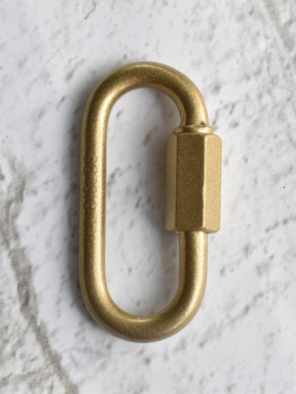 Close-up of a 3/16 inch quick link metal connector with threaded screw lock, resting on a textured background.