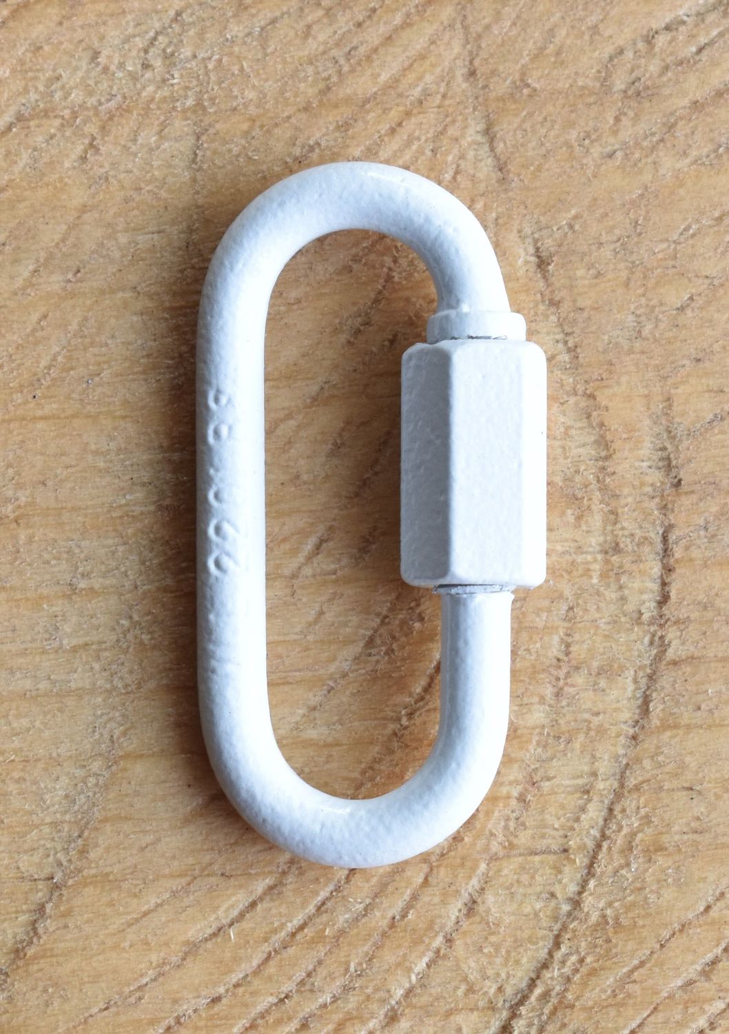 Close-up of a 1/8 inch quick link metal connector with threaded screw lock, shown on a wooden surface.