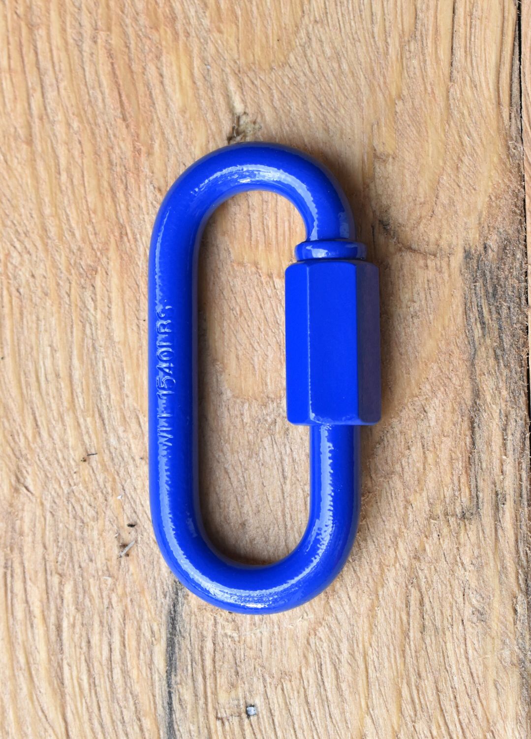 Close-up of a 5/16 inch quick link metal connector with threaded screw lock, resting on a wooden surface.