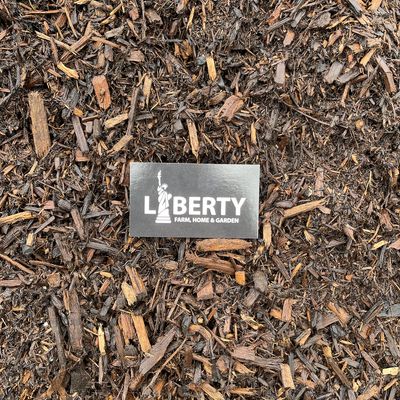 Close-up of natural brown hardwood mulch with a Liberty Farm, Home &amp; Garden card