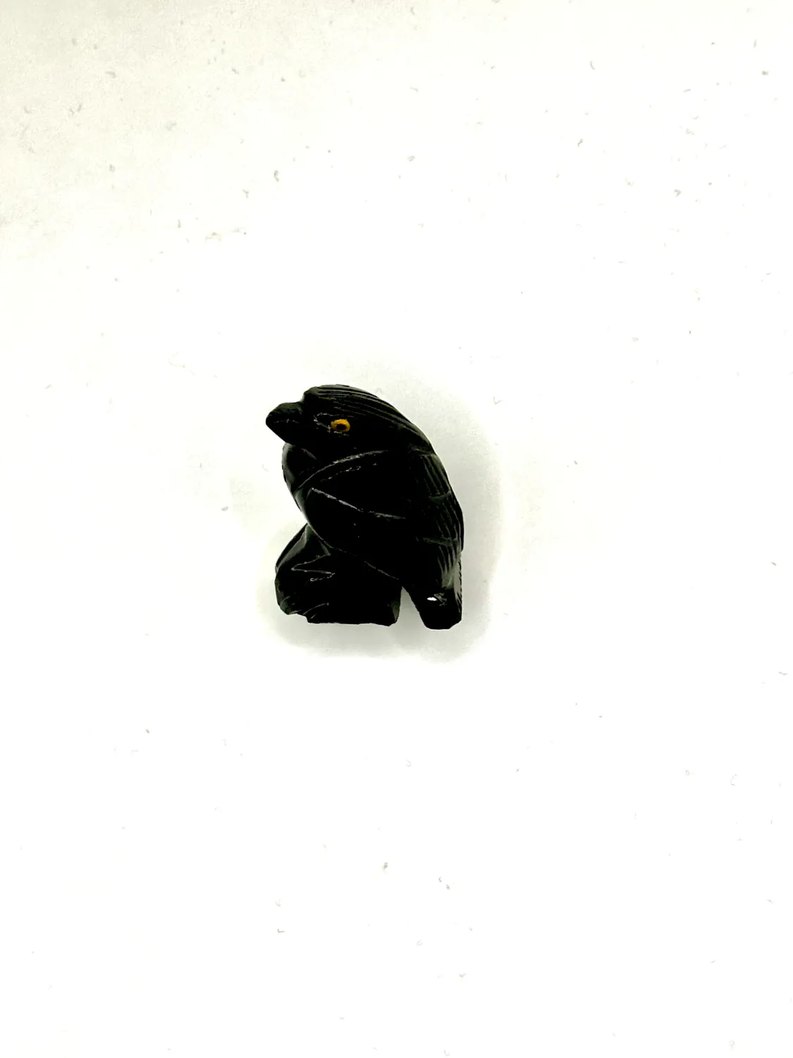 Black onyx raven carving with carved feathers and an amber eye, on a white surface.
