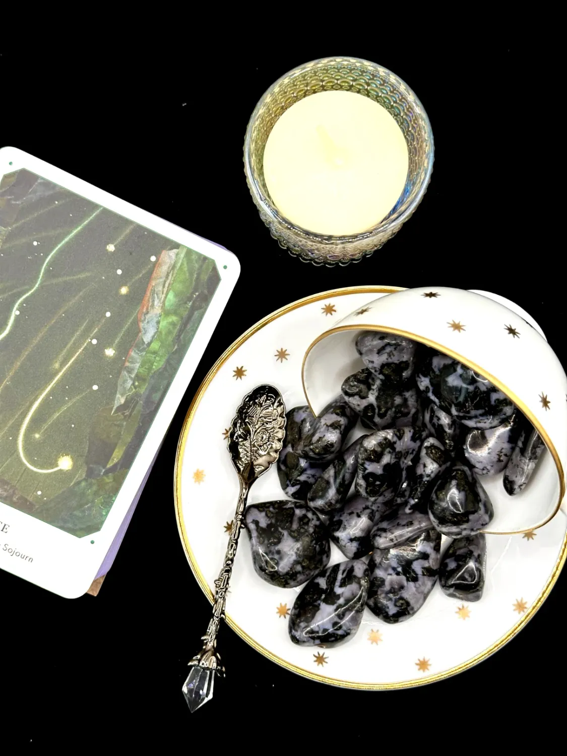 Indigo gabbro tumbled stones in black with gray-lavender mottling spilling from a tipped white teacup onto a saucer.