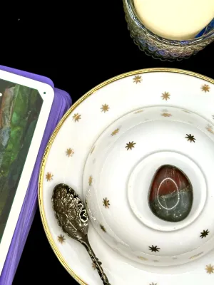 African bloodstone tumbled stone, deep red on top and gray-green below, on a white teacup and saucer with gold stars.