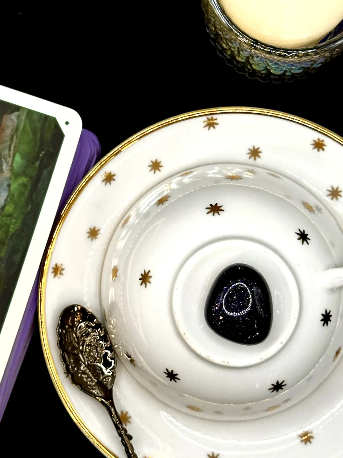 Deep navy blue goldstone tumbled stone flecked with glitter on a white teacup and saucer with gold stars.