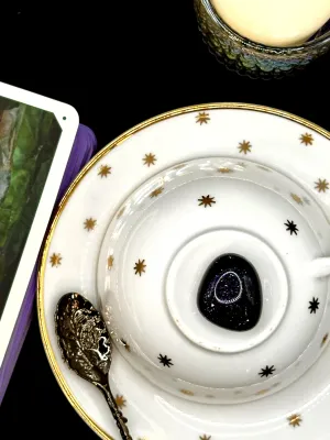 Deep navy blue goldstone tumbled stone flecked with glitter on a white teacup and saucer with gold stars.