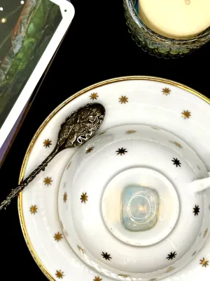 Milky translucent opalite tumbled stone with a soft blue glow on a white teacup and saucer with gold stars.