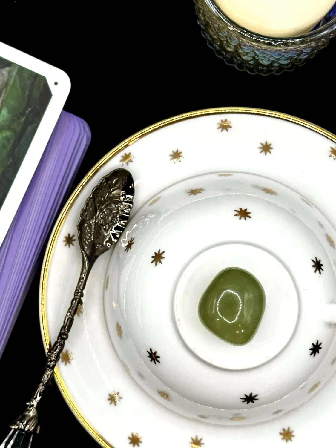 Translucent olive green healerite tumbled stone on a white teacup and saucer with gold stars.