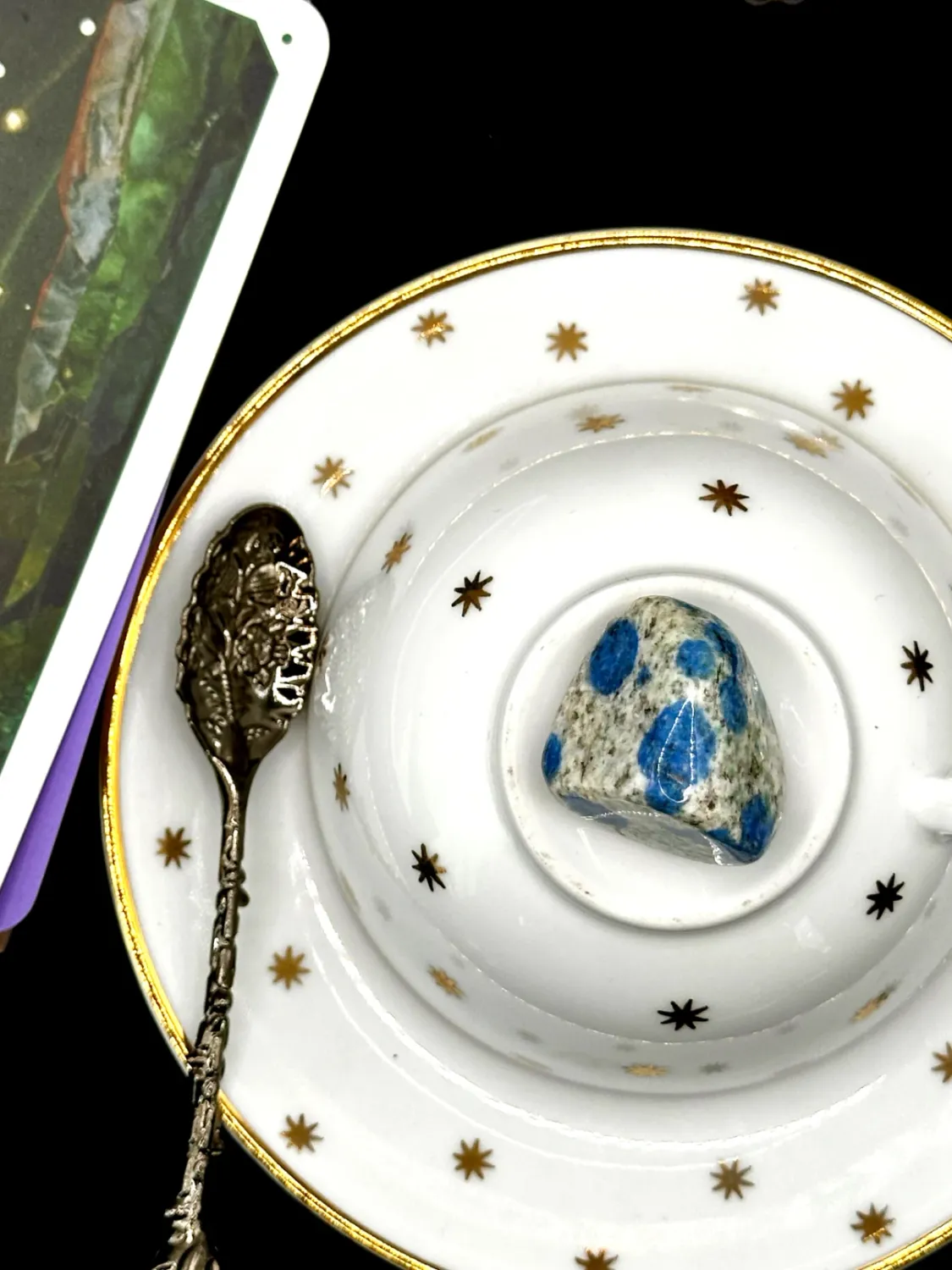K2 tumbled stone, white and gray speckled with bright blue spots, on a white teacup and saucer with gold stars.