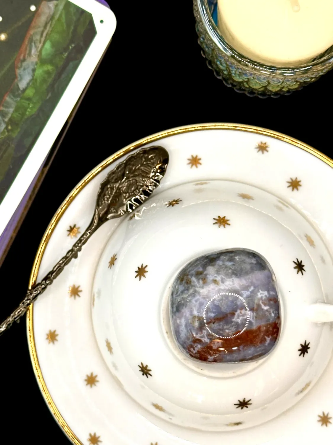 Ocean jasper tumbled stone in blue-gray and white with a rust red band on a white teacup and saucer with gold stars.