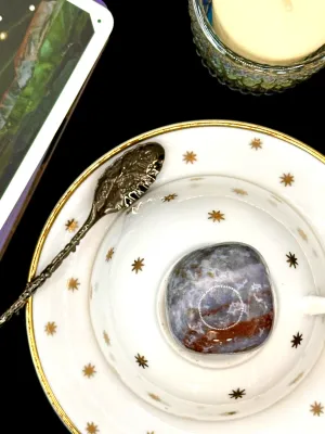 Ocean jasper tumbled stone in blue-gray and white with a rust red band on a white teacup and saucer with gold stars.