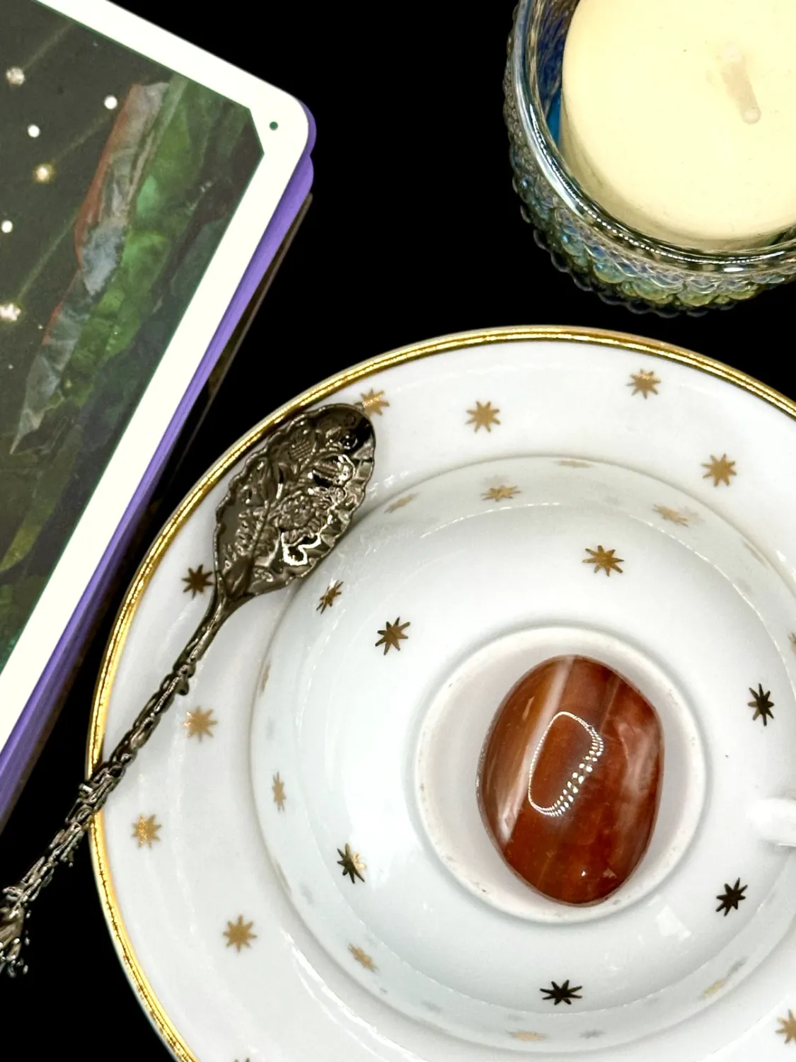 Red sardonyx tumbled stone in deep orange-red with faint white banding on a white teacup and saucer with gold stars.