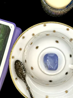 Soft periwinkle blue lace agate tumbled stone on a white teacup and saucer with gold stars.