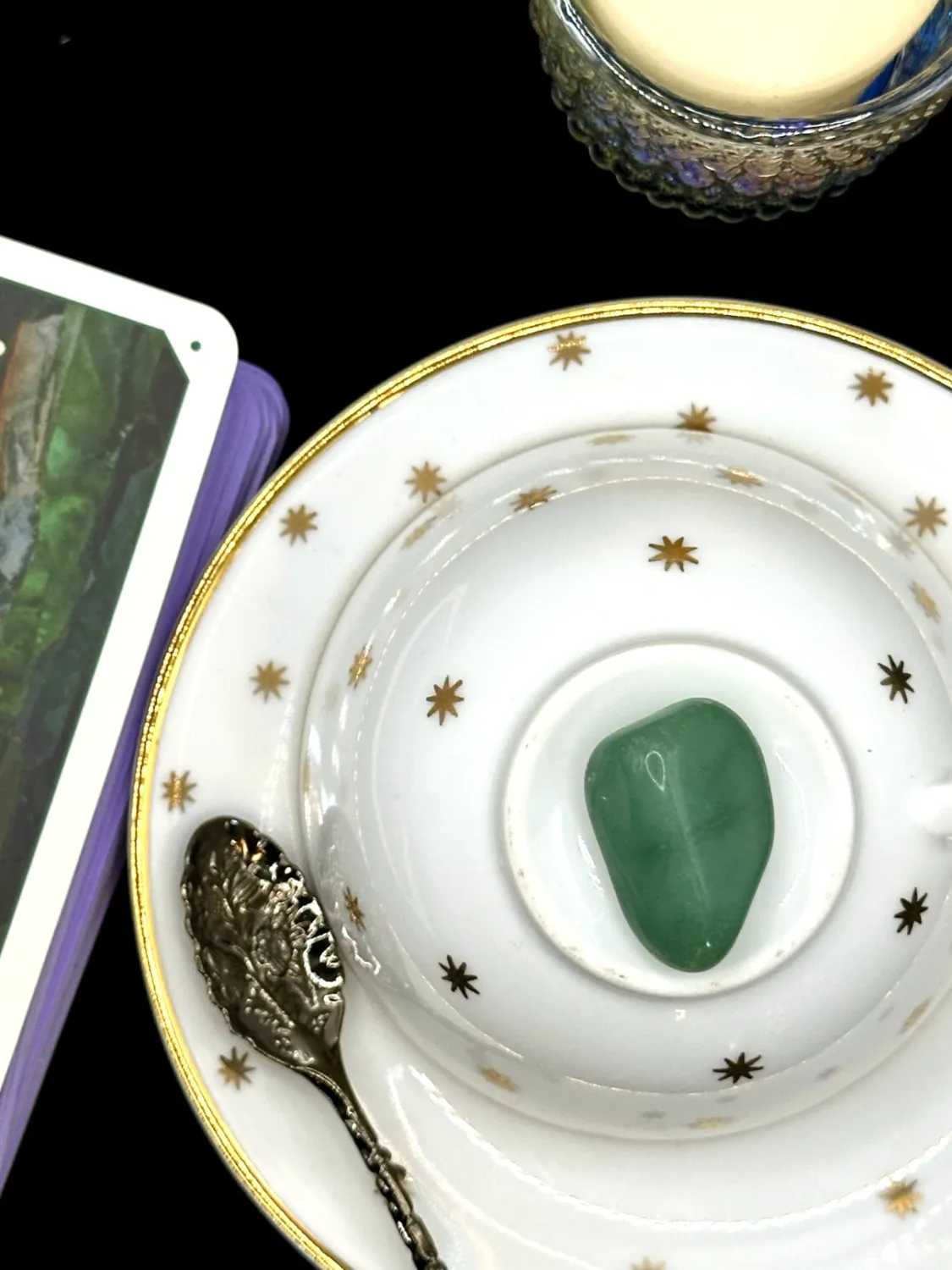 Pale blue-green aquamarine tumbled stone with soft white clouding on a white teacup and saucer with gold stars.