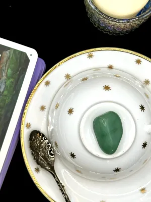 Pale blue-green aquamarine tumbled stone with soft white clouding on a white teacup and saucer with gold stars.